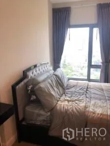 Condominium for rent or sale in Khlong Toei, Bangkok - Bedroom side view showing upholstered bed and floor-to-ceiling window.