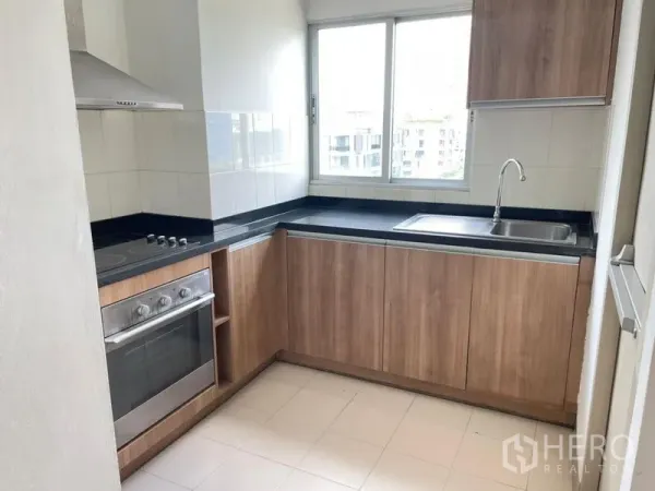 Condominium for rent in Khlong Toei, Bangkok - Windowed U-shaped kitchen with wood cabinets, electric cooktop, oven, and black countertops.