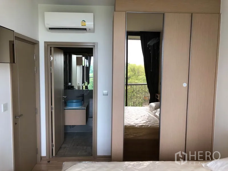 Condominium for rent in Watthana, Bangkok - Bedroom corner with mirrored wardrobe, air conditioner and doorway to the bathroom.