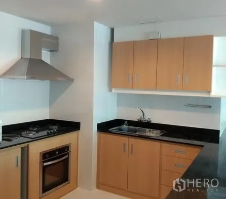 Apartment for rent in Pathum Wan, Bangkok - Fitted kitchen with oven, cooktop, range hood, wood cabinetry and black countertops.