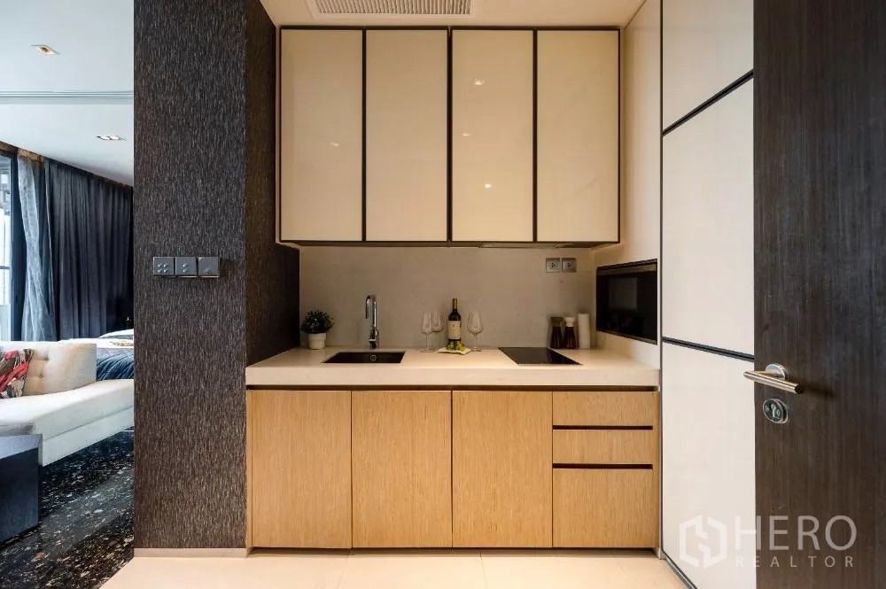 Condominium for rent or sale in Khlong Toei, Bangkok - Front view of kitchenette with induction hob, upper cabinets and sleek backsplash.