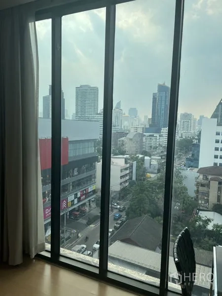 Condominium for rent or sale - High-floor city view from tall window overlooking shops and towers.