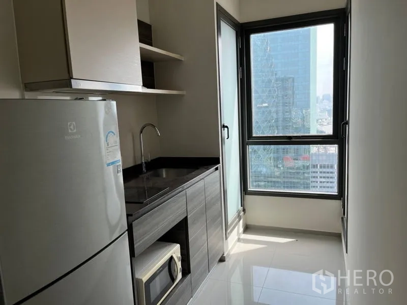 Condominium for sale in Phaya Thai, Bangkok - Compact kitchen with cabinets, sink, fridge and big corner windows with skyline view.