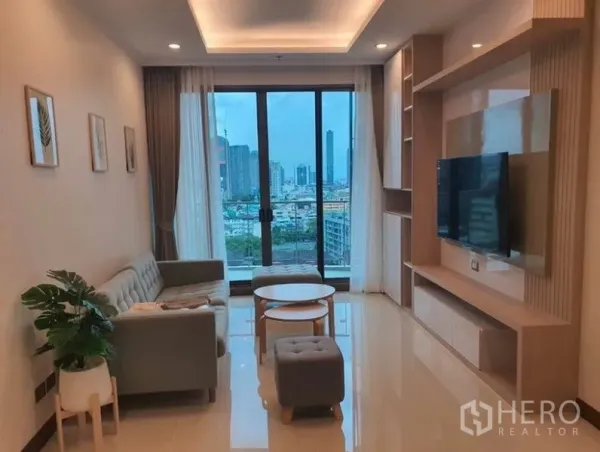 公寓 出租在Watthana, Bangkok - 明亮客厅，内置电视墙与沙发组，落地窗可眺望曼谷天际线。