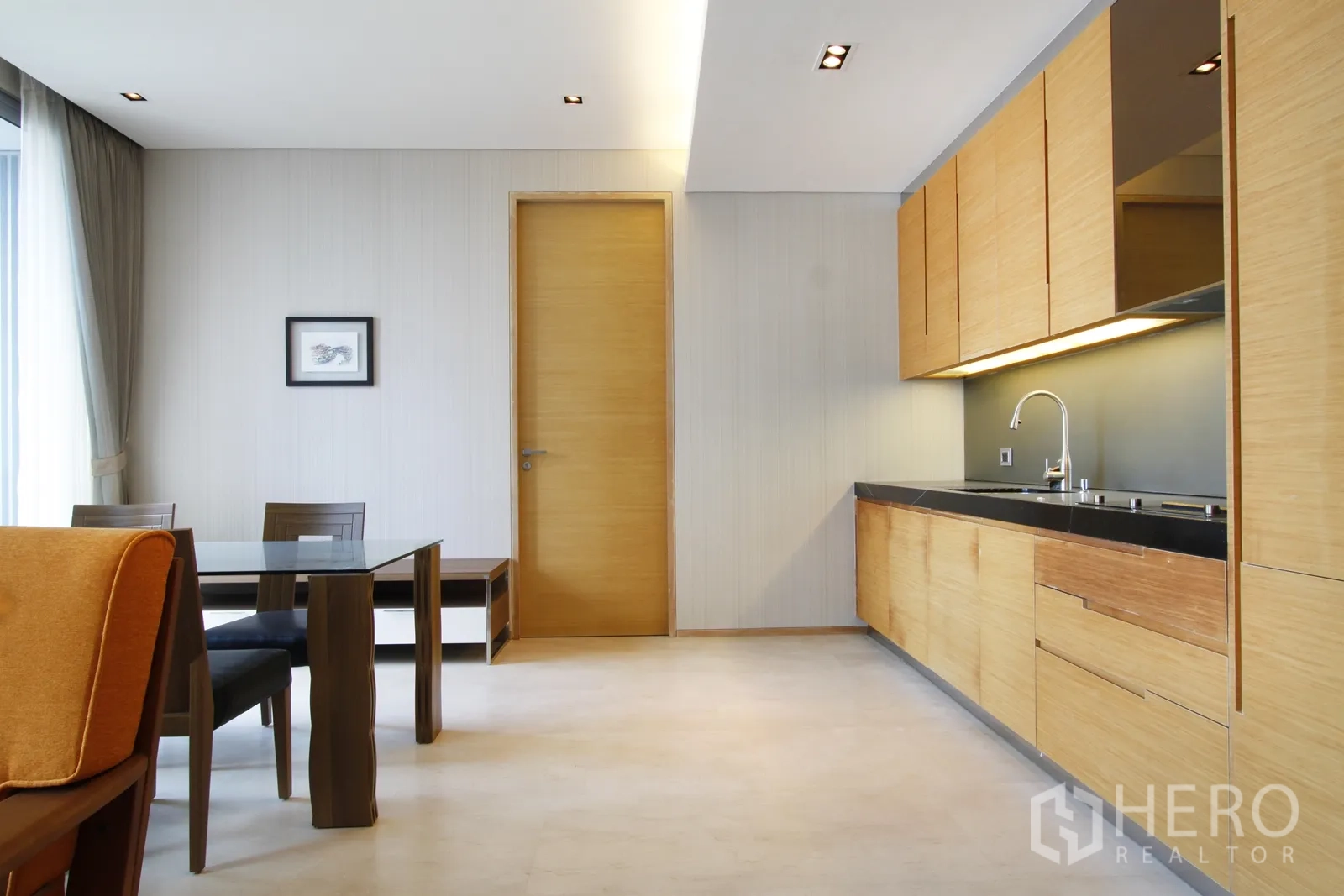 Condominium for sale in Bang Rak, Bangkok - Open-plan living with glass dining table and light wood kitchenette with black stone countertop.
