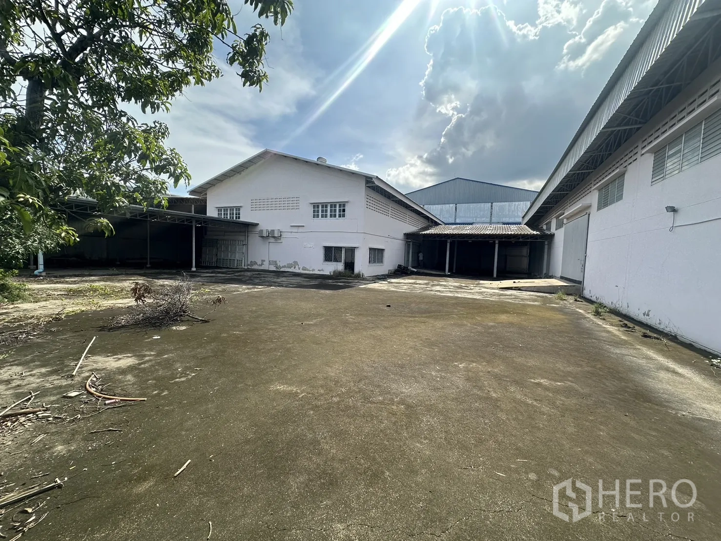 Factory for rent or sale in Prawet, Bangkok - Large concrete yard between two warehouse buildings with covered loading bays and trees.