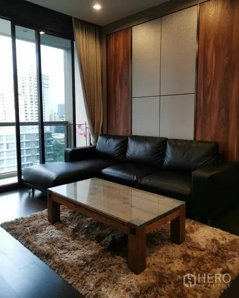 Condominium for rent or sale in Watthana, Bangkok - Living room with black leather sectional, glass coffee table and balcony city view.