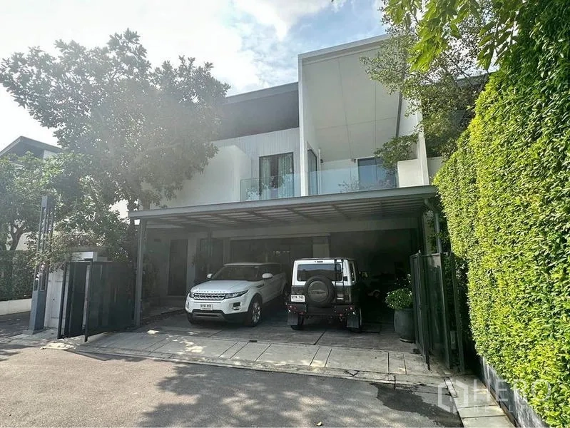 Townhouse for rent or sale in Bang Phli, Samut Prakan - Street view of modern townhouse with covered parking for multiple cars and trimmed hedge.