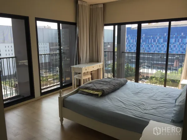 Condominium for rent or sale in Watthana, Bangkok - Corner bedroom wrapped in floor‑to‑ceiling windows showcasing urban skyline views near BTS Ekkamai.