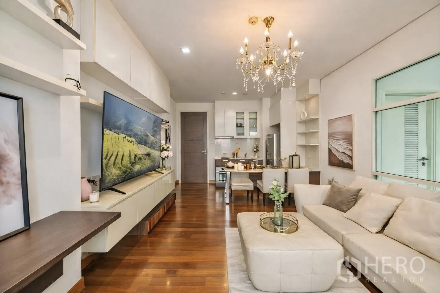 คอนโด for rent or sale in Watthana, Bangkok - พื้นที่นั่งเล่นแบบเปิดโล่งมีโคมระย้า โซฟา และทีวี เชื่อมต่อครัวและมุมทานอาหาร