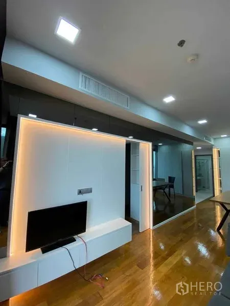 Condominium for rent or sale in Khlong Toei, Bangkok - Living area with LED-lit feature wall, TV unit, mirrored panels and glossy hardwood floors.