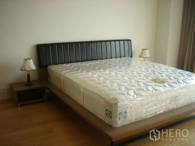 Condominium for rent in Sathon, Bangkok - Spacious bedroom with king bed, black headboard and bedside lamps.