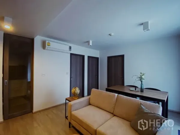Condominium for rent in Pathum Wan, Bangkok - Living area showing three wooden doors, wall air-conditioner, sofa and dining table.