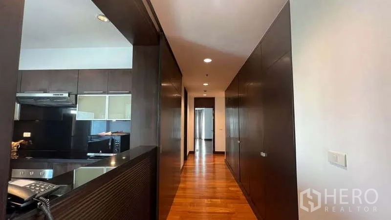 房间 出租在Pathum Wan, Bangkok - 厨房一侧的长走廊，内置深色收纳柜与木地板。