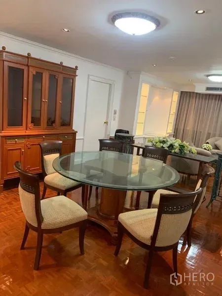 Condominium for sale in Watthana, Bangkok - Dining zone with a round glass table and six upholstered chairs beside a display cabinet.