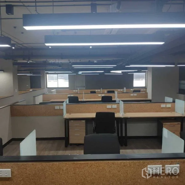 Office Space for rent - Rows of cubicles beneath suspended strip lights with windows at the far end.