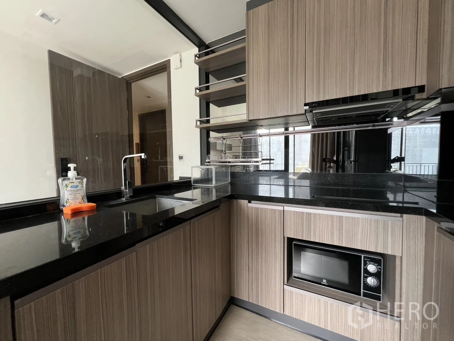 คอนโด for rent in Watthana, Bangkok - ภาพระยะใกล้ของท็อปหินสีดำ พร้อมอ่างล้างจานและตู้ไม้ในครัว.