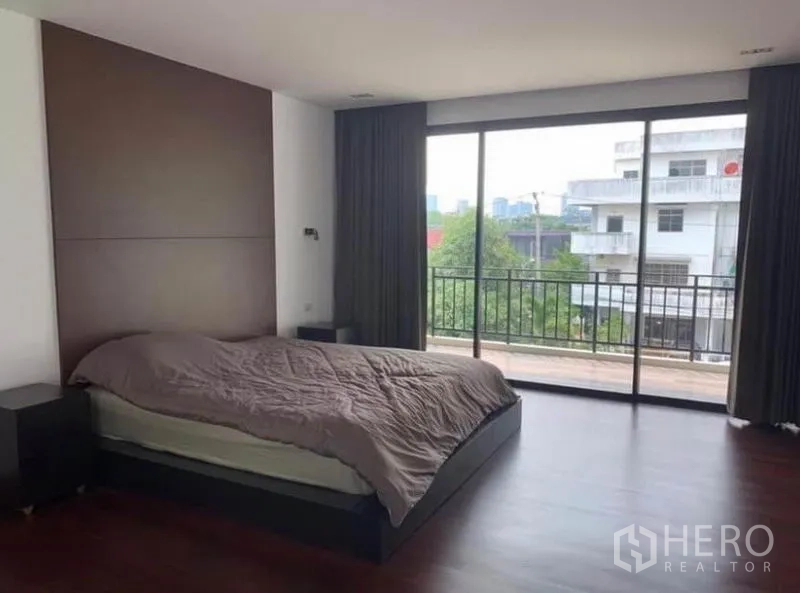Townhouse for rent in Din Daeng, Bangkok - Spacious master bedroom with wood floors and sliding glass doors opening to a balcony with neighborhood view.