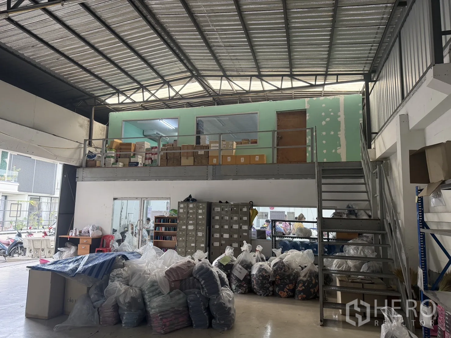 Warehouse for rent in Suan Luang, Bangkok - Mezzanine room above ground workspace with metal stairs and boxes arranged for storage.