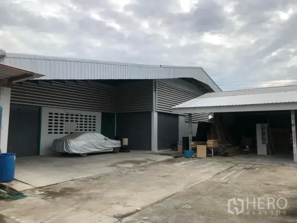 Warehouse for rent in Mueang Pathum Thani, Pathum Thani - Metal-clad warehouse exterior with roller shutter doors, covered loading bay, and a large concrete yard for truck access and parking.