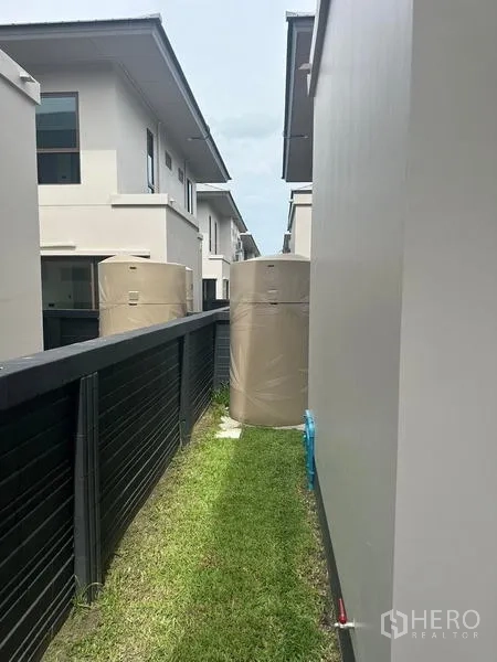 独立式住宅 出租在Bang Kapi, Bangkok - 侧庭狭长草地，围栏旁放置蓄水罐与管线。