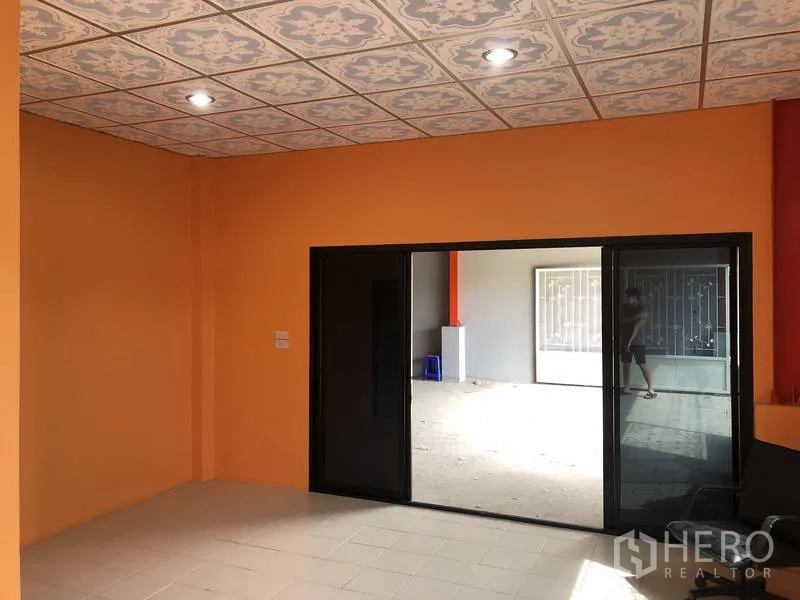 คลังสินค้า ให้เช่าในNonthaburi - ออฟฟิศชั้นล่างผนังสีส้ม เพดานลาย และประตูกระจกบานเลื่อนสีดำเปิดสู่ตัวโกดัง
