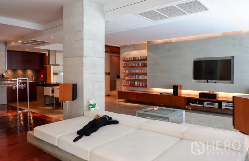 Condominium for rent or sale in Khlong Toei, Bangkok - Contemporary living room with large sectional sofa and custom media wall beside the open kitchen.
