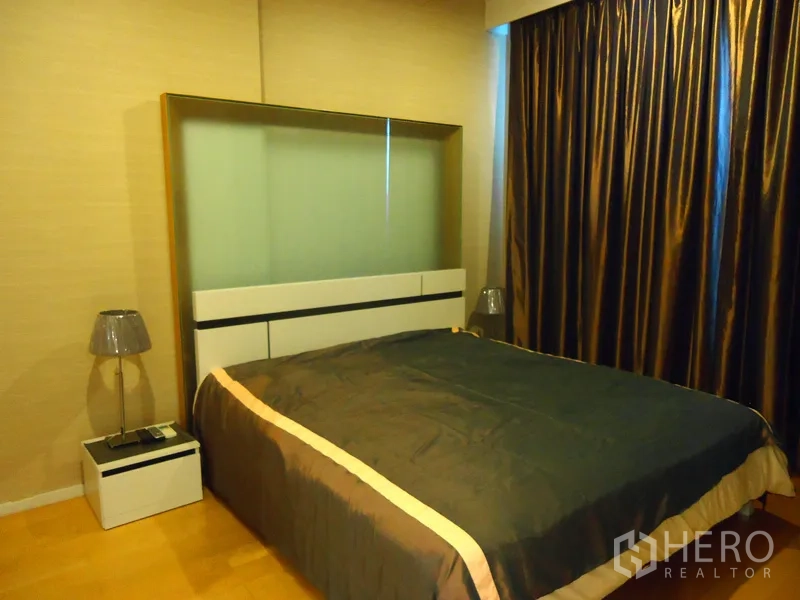 Condominium for rent in Chatuchak, Bangkok - Cozy bedroom with large bed, bedside tables and blackout curtains in warm tones.
