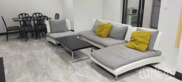 Condominium for rent in Watthana, Bangkok - Two modern chaise sofas with yellow cushions beside dining set and kitchen entrance.