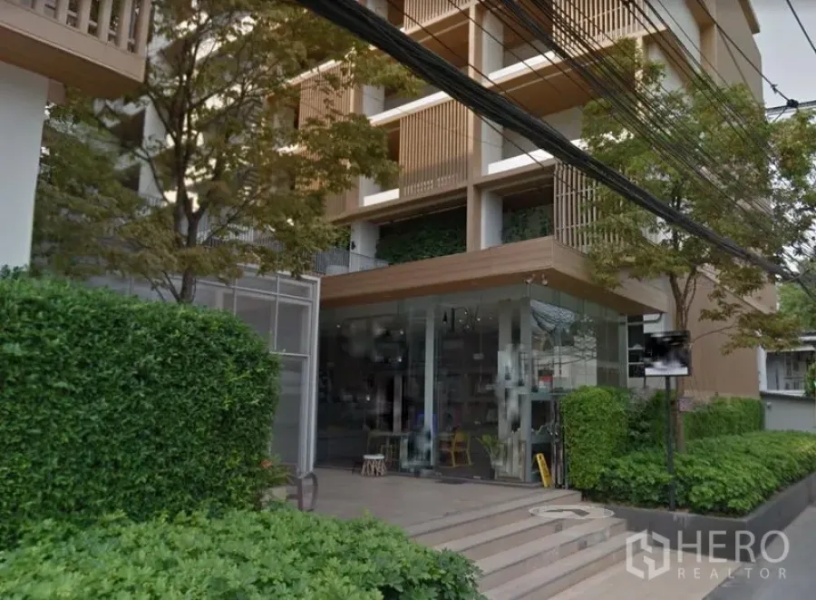 零售空间 出租在Watthana, Bangkok - 建筑外观，现代立面与转角玻璃店铺、修剪整齐的绿篱。