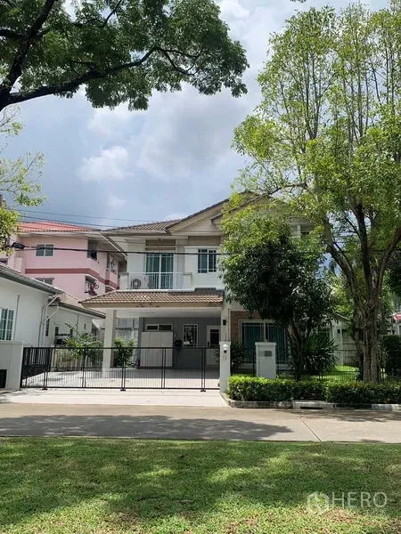 Detached House for rent in Bang Kapi, Bangkok - Front elevation of a gated two-storey house with driveway on a leafy street.