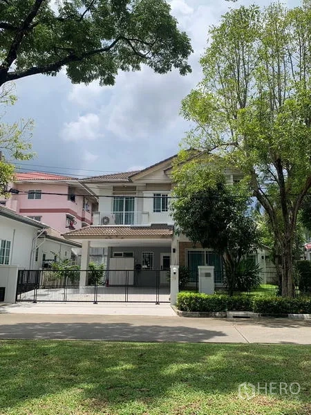 Detached House for rent in Bang Kapi, Bangkok - Front elevation of a gated two-storey house with driveway on a leafy street.