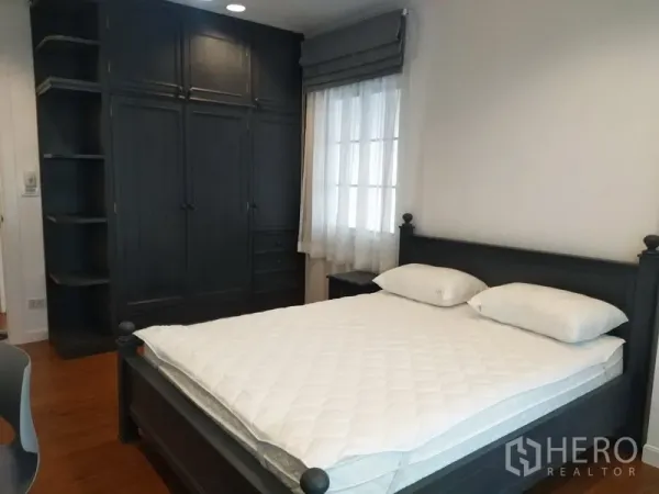 Townhouse for rent in Mueang Samut Prakan, Samut Prakan - Bedroom with dark wood bed, built‑in wardrobe, and window with sheer curtains.