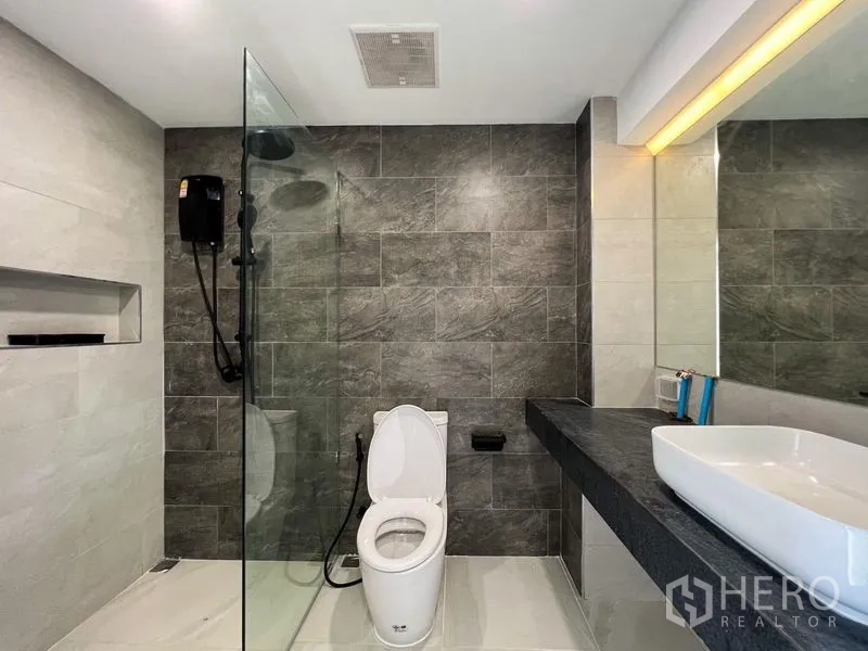 Townhouse for rent or sale - Modern bathroom with glass shower, dark stone accent wall and long vanity.