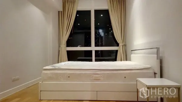 Condominium for rent or sale in Khlong Toei, Bangkok - Minimalist master bedroom with large window, curtains, queen bed and bedside table overlooking city lights.