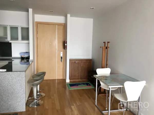 Condominium for rent or sale in Khlong Toei, Bangkok - Entrance and dining nook with wooden floors, breakfast bar and two stools beside the kitchen.