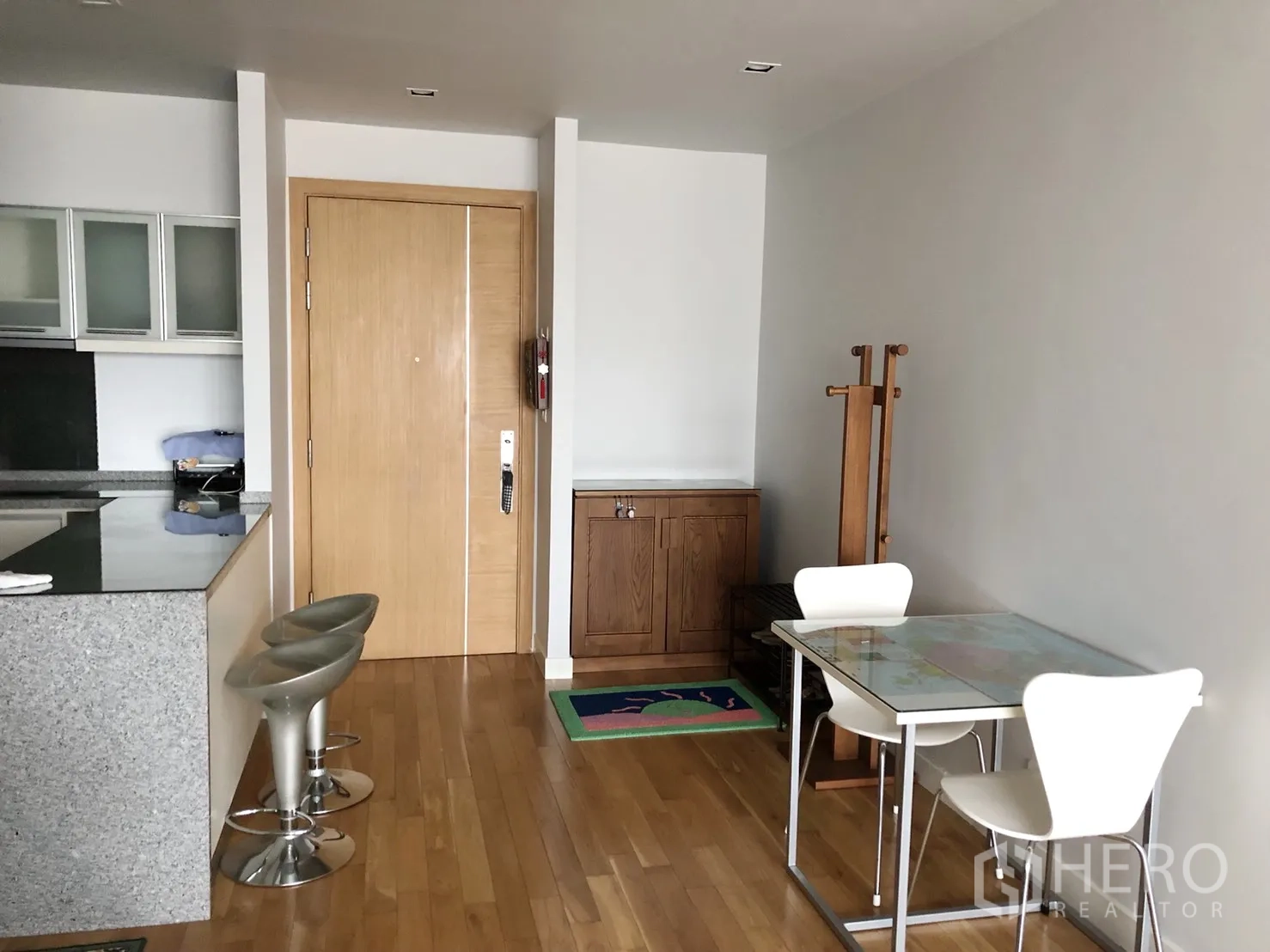 Condominium for rent or sale in Khlong Toei, Bangkok - Entrance and dining nook with wooden floors, breakfast bar and two stools beside the kitchen.