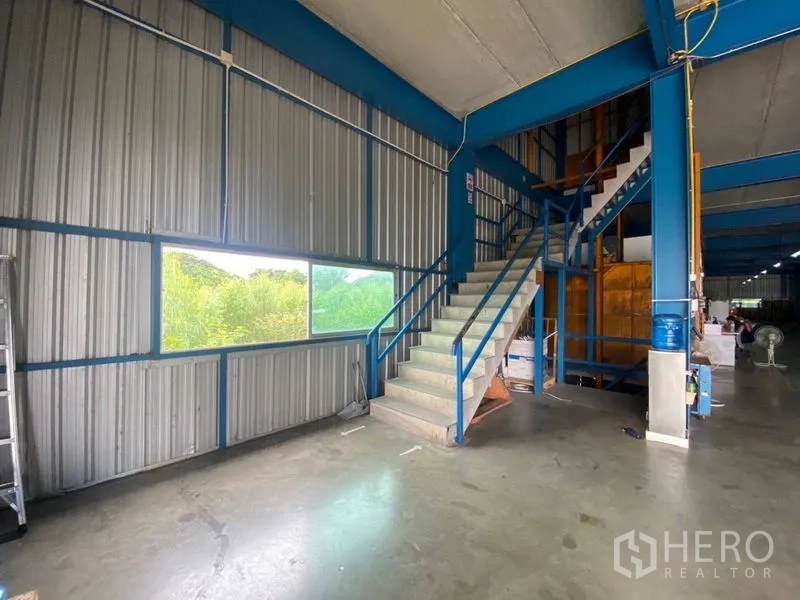 Factory for rent or sale in Lam Luk Ka, Pathum Thani - Metal-clad interior with staircase to a mezzanine and a large side window.