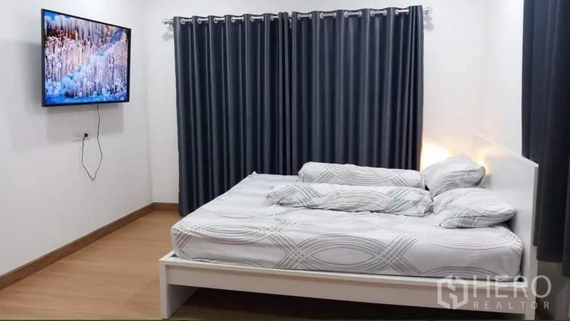 独立式住宅 出租或出售在Prawet, Bangkok - 明亮卧室，白色床架、壁挂电视与深色遮光窗帘