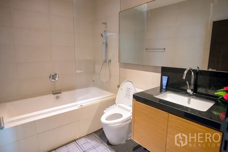 คอนโด ให้เช่าในWatthana, Bangkok - ห้องน้ำสมัยใหม่พร้อมอ่างอาบน้ำและฝักบัว กั้นกระจก กระจกบานใหญ่ และเคาน์เตอร์ท็อปหินสีดำ
