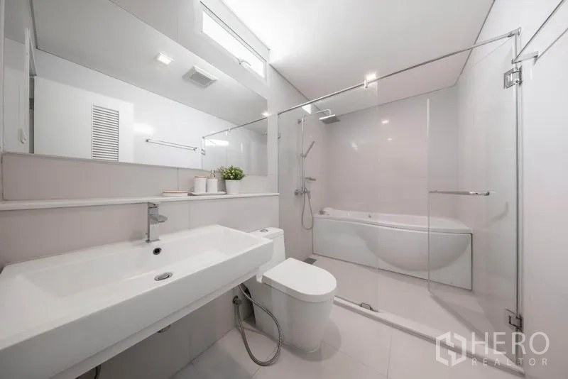 Condominium for rent in Watthana, Bangkok - Contemporary bathroom with long vanity, toilet, glass shower, and bathtub.
