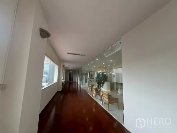 Retail Space for rent in Watthana, Bangkok - Bright corridor with polished wooden floor and a glass-walled retail unit featuring seating and ceiling lights in a Bangkok building.