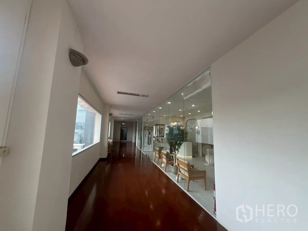 Retail Space for rent in Watthana, Bangkok - Bright corridor with polished wooden floor and a glass-walled retail unit featuring seating and ceiling lights in a Bangkok building.