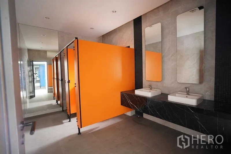 Standalone for rent in Bang Na, Bangkok - Restroom corridor with orange partitions and dual sinks on a black counter.