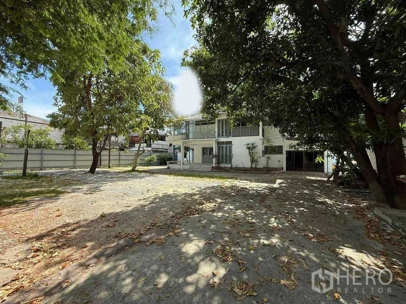 Detached House for rent in Watthana, Bangkok - Spacious tree‑shaded front yard leading to a white two‑storey detached house.