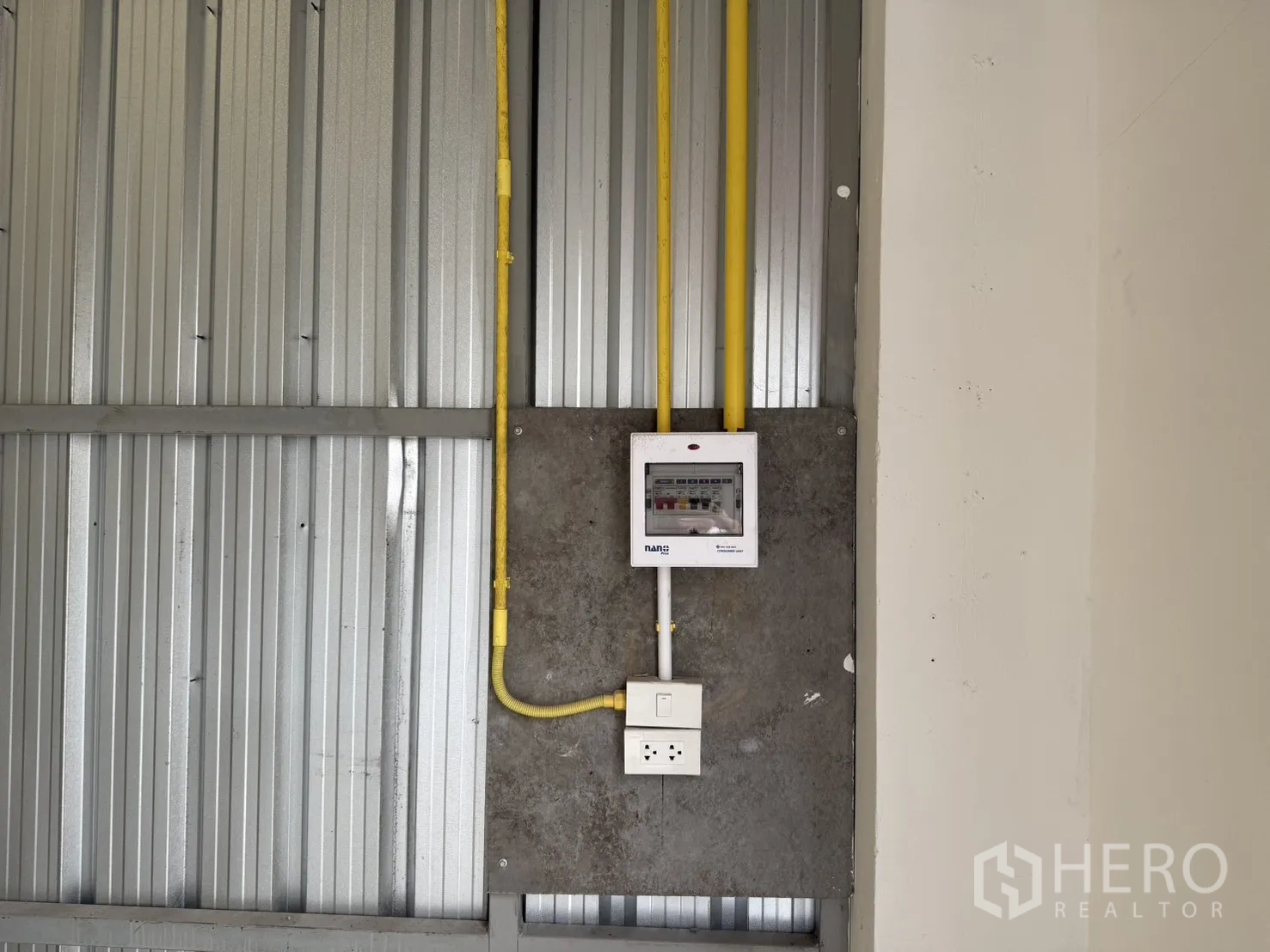 Warehouse for rent in Suan Luang, Bangkok - Close-up of the interior electrical panel with yellow conduit and a power outlet on a corrugated metal wall.