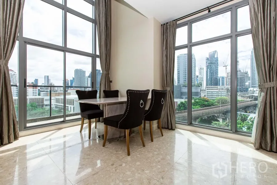 公寓 出租在Khlong Toei, Bangkok - 转角餐区配大理石餐桌与四把椅子，落地窗外可见曼谷天际线与轻轨轨道。