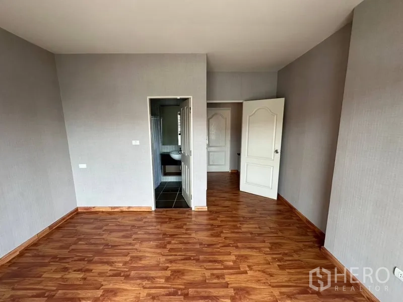Townhouse for rent or sale in Phra Khanong, Bangkok - Bedroom with wood floors, neutral walls, and doorway to ensuite.