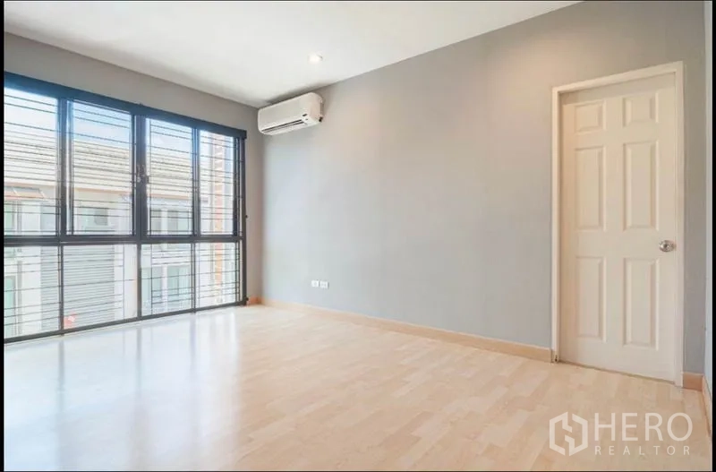 Townhouse for sale in Khlong Toei, Bangkok - Sunlit bedroom with large corner windows, air conditioner and light wood flooring.