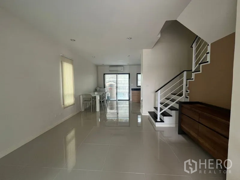 Townhouse for rent in Bang Kapi, Bangkok - Open-plan living and dining area with glossy tiles and staircase to upper floors.